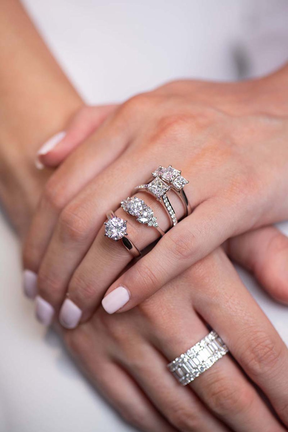 Womans hands with a range of sterling silver diamond engagement rings and diamond encrusted wedding band on other hand from Tom Coll Jewellery